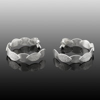 Hand-fabricated, sterling silver post hoops of textured and shiny leaves.