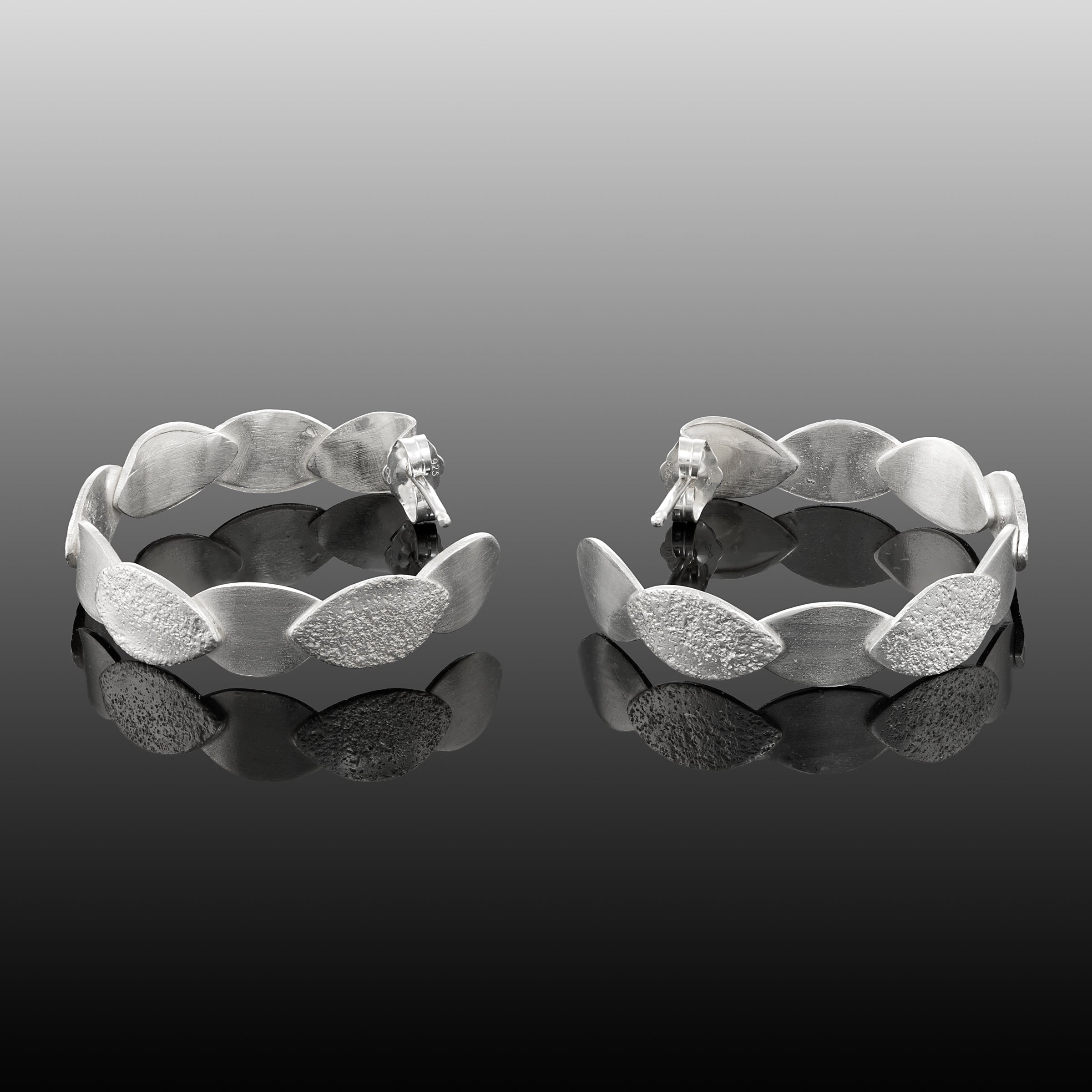 Hand-fabricated, sterling silver post hoops of textured and shiny leaves.