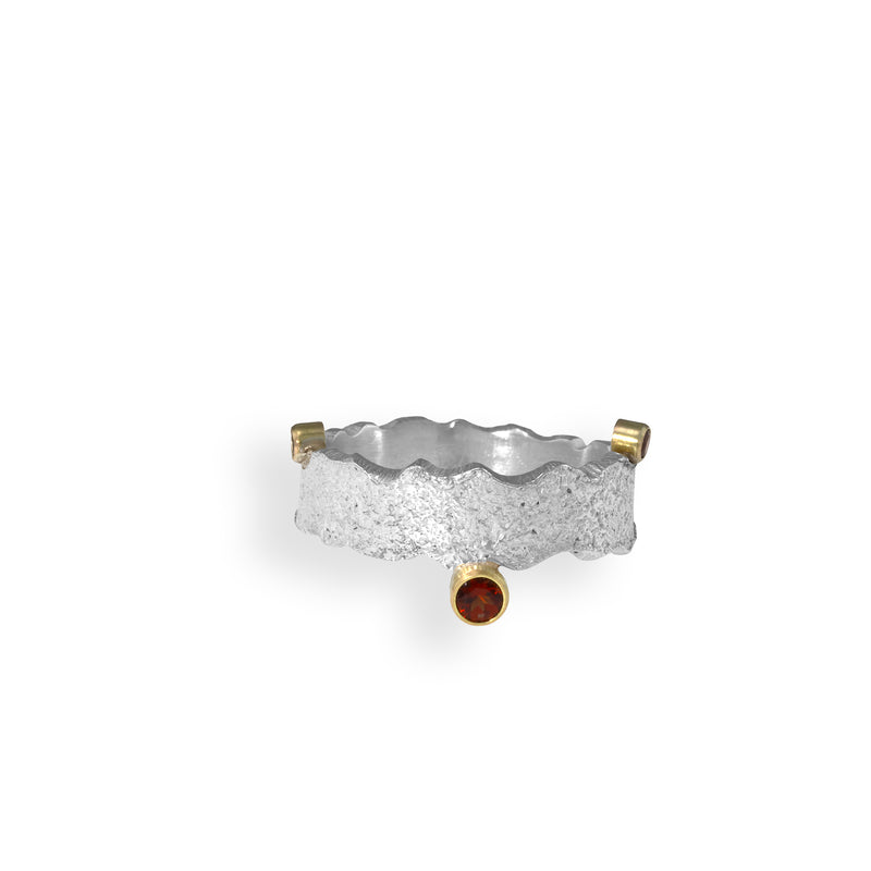 Hand-crafted contemporary ring of hammered sterling silver featuring three red garnets set in 14k gold bezels.
